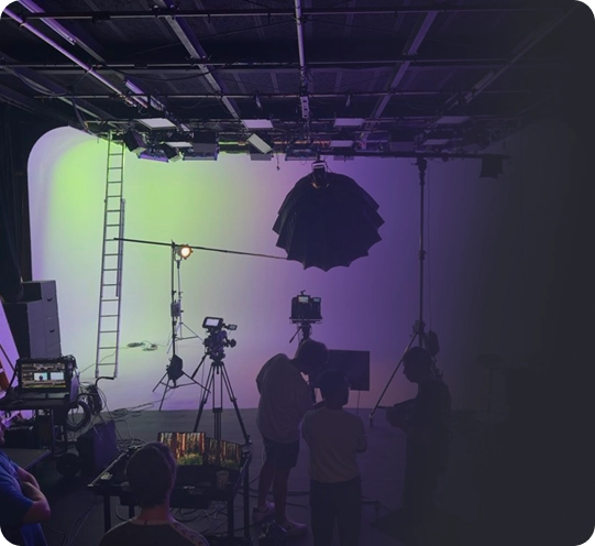 Filmstudio met crew die zich aan het voorbereiden is. Helder verlichte achtergrond in kleurovergangen, camera's en verlichtingsapparatuur in beeld. Drukke, collaboratieve sfeer.