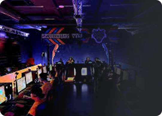 Slecht verlichte gamingarena met neonblauwe en oranje lampen. Rijen spelers achter computerstations, gefocust op hun schermen. Energieke, competitieve sfeer.
